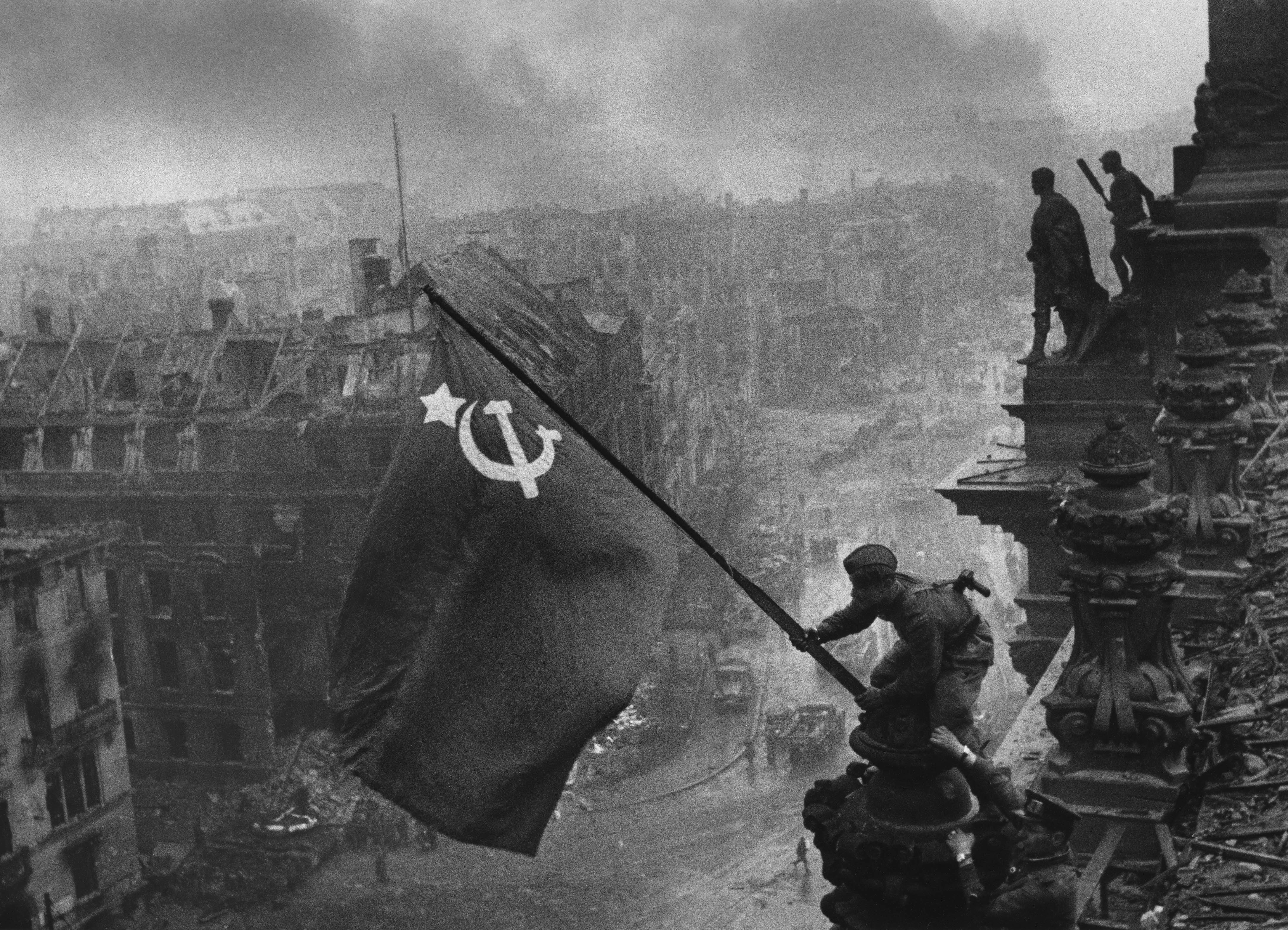Two soldiers raise the USSR flag above the smoky skies of Berlin