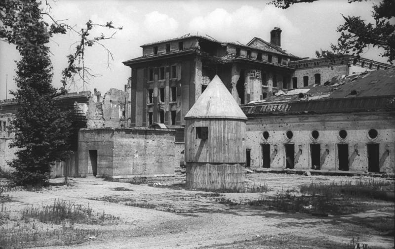 Signs of war and wrecked buildings stand around the chancellery. 