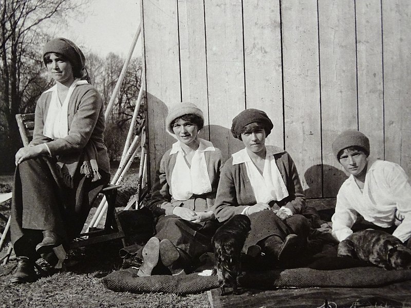 All four sisters dress similar outfits in caps while they bask in the sun. Two of their dogs sit at their feet